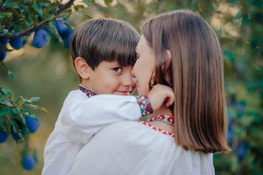 Tender scene of loving son embracing mom on plum orchard backdrop with sunlight. Beautiful family. Cute 4 years old kid with mother. Parenthood, childhood, happiness, children wellbeing concept.