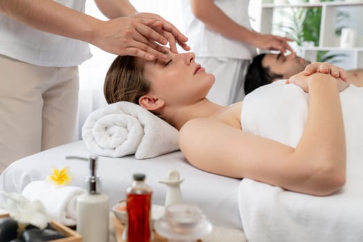 Caucasian couple enjoying relaxing anti-stress head massage and pampering facial beauty skin recreation leisure in dayspa modern light ambient at luxury resort or hotel spa salon. Quiescent