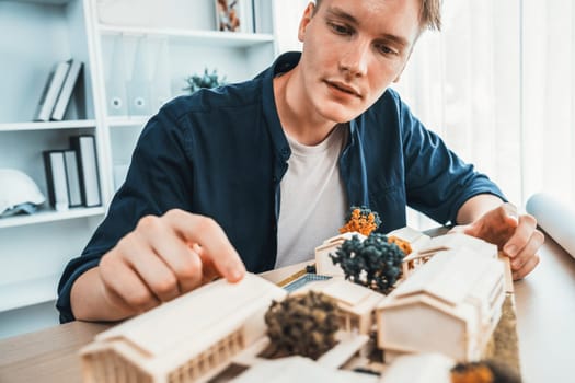 Architect designer studies elegant house model, reviewing structure design for improvement with construction plan on table. Creativity and innovation in architectural design. Iteration