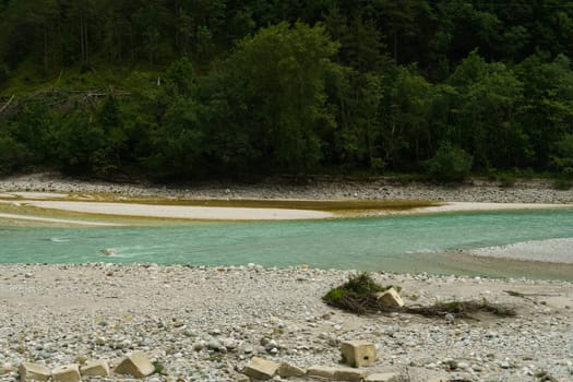 Clear turquoise water flows gently around golden sandy banks, flanked by smooth stones and vibrant green foliage, inviting a sense of calm and connection with nature.