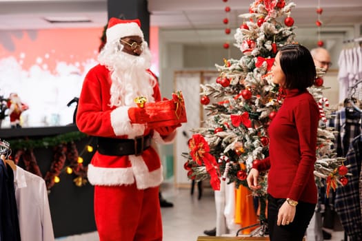 Employee in Santa Claus suit starting raffle contest with box, giving clients chance to win discounts in festive store. Man dressed in costume invites people to participate in fun holiday activity.