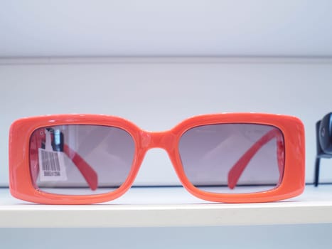 Pair of orange sunglasses sits on a white shelf, showcasing its modern design and vibrant color. The sunglasses are ready to be tried on by a stylish customer