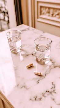 Two glasses of water stand ready beside a pair of medical capsules on a marble tabletop, evoking themes of wellness, medication, and hydration