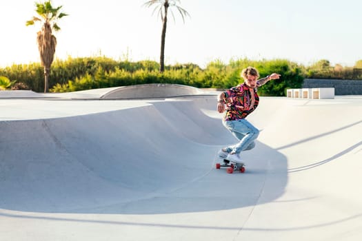 front view of anonymous funky young male skateboarder in trendy colorful shirt and jeans performing trick on concrete ramp while practicing skills in skatepark