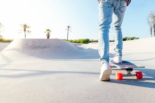 unrecognizable stylish skater in jeans and sneakers riding a skateboard in skatepark on sunny day in summer