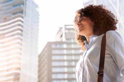 portrait of a smiling female entrepreneur in smart casual outfit walking along street in megalopolis and looking away