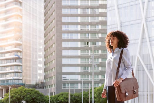 serious female entrepreneur in smart casual outfit standing at street in megalopolis and looking away