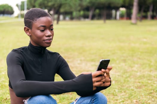 young african american young woman in casual apparel smiling happy using mobile phone in a park, concept of technology of communication and young lifestyle