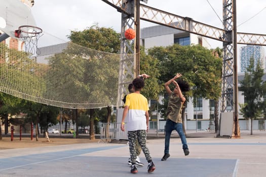 three focused multiethnic teen friends having fun playing basketball on sports ground in city park, concept of youth and urban lifestyle