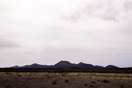 scenery view of volcano Cuervo and rough mountains under cloudy sky in Tinajo, Lanzarote at Canary Islands Spain, concept of dry landscape and adventure travel
