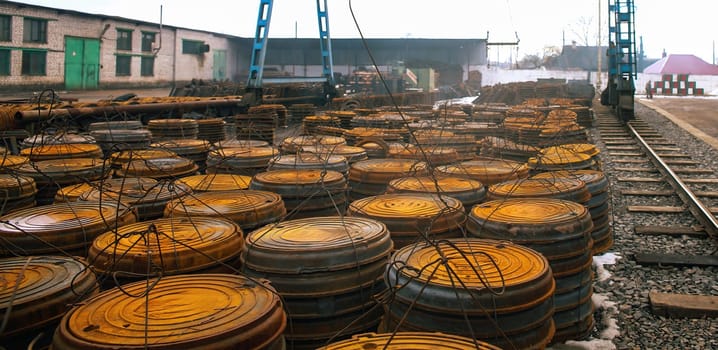 A collection of large, round metal containers is stacked densely in an industrial storage area next to railway tracks, illuminated by soft morning light.