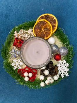 festive Christmas arrangement featuring a lit candle, dried oranges, ornaments, and holiday decorations on a blue background. holiday season and warm inviting atmosphere. Celebration and xmas decoration concept