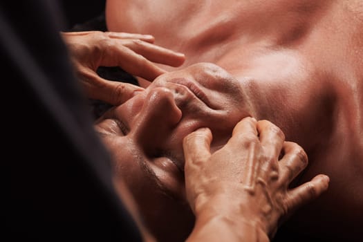 girl masseur doing facial massage to man on dark background close-up, facial skin rejuvenation, relaxation and meditation