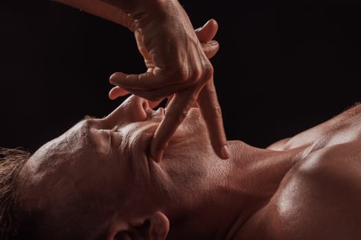 girl masseur doing facial massage to man on dark background close-up, facial skin rejuvenation, relaxation and meditation