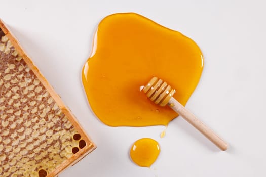spoon with spilled honey and bee honeycomb on white background, top view, beekeeping concept