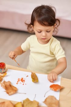 happy little child girl painting autumn leaves. baby girl drawing leaves in yellow and orange paint