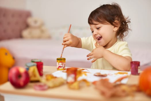 happy little child girl painting autumn leaves. smiling baby girl drawing leaves in yellow paint