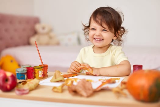 happy little child girl painting autumn leaves. baby girl drawing leaves in yellow and orange paint