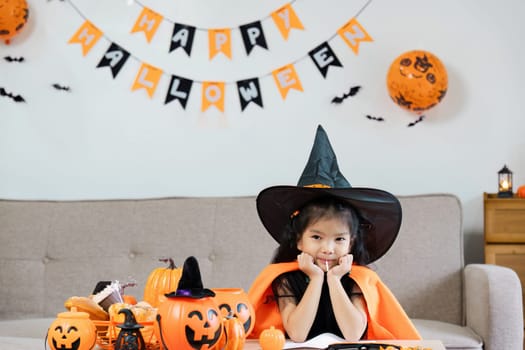 Adorable child dressed as a witch enjoying Halloween festivities with pumpkins and decorations in a cozy indoor setting.