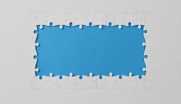 Top view of white puzzle frame with missing pieces in middle, empty space in centre. Missing details, unfinished composition. Game, jigsaw, entertainment concept