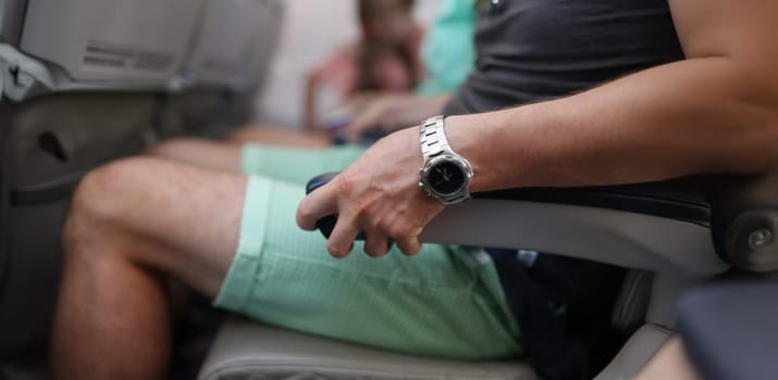 Close-up of male person seat in airplane and squeezes chair, scared to fly in sky. Person trying to control emotions. Aerophobia and panic attacks concept