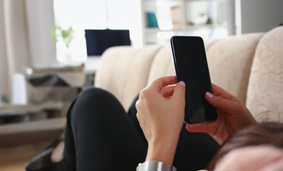 Close-up of female laying on couch with smartphone turned off black screen. Woman hold blocked device, resting on sofa at home. Technology, mockup concept