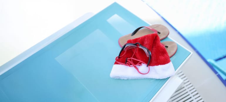 Hat of Santa Claus, swimming slippers on sunbed. Holidays near sea pool for Christmas holidays and relaxation, leisure, tourism concept.