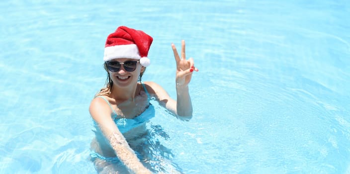 Young smiling woman in santa claus hat in pool. Winter Holidays tourism and recreation concept