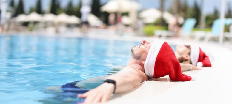Young people in santa claus hats lie relaxed in pool. Tourism vacation for New Year holidays concept