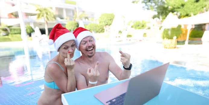 Man and woman in santa claus hats show fucking gesture into monitor. Remote work and rest in quarantine concept