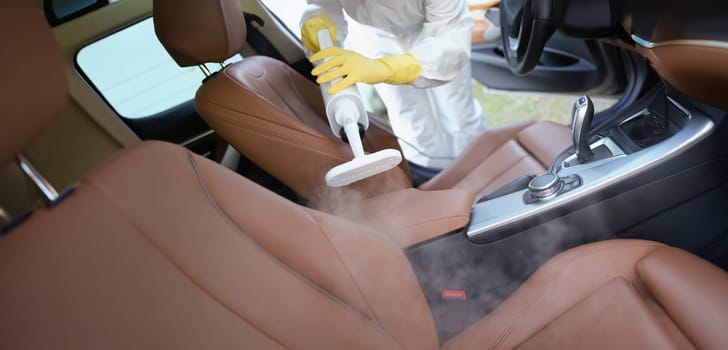 Close-up of hazmat worker cleansing car interior with spray disinfectant and steam heat. Disinfect auto upholstery from virus. Covid prevention concept