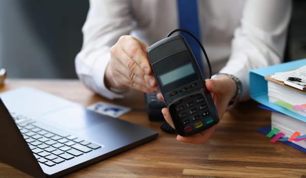 Close-up of man holding modern credit card reader machine for cashless payment. Empty screen for total cost and numbers on pad. Modern technology concept