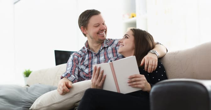 Portrait of middle aged father and young daughter reading book together sitting on couch at home. Happy emotion and quality time together. Family concept