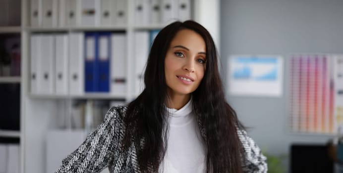 Portrait of attractive young businesswoman wearing stylish jacket posing in company office. Brunette corporate worker smiling. Business, career concept