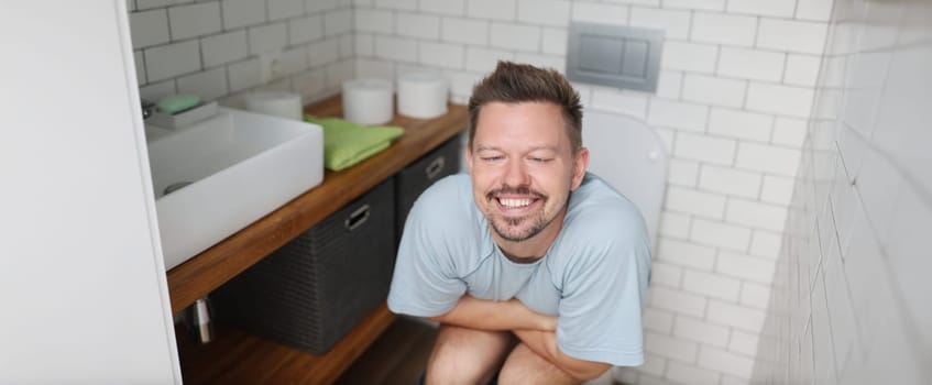 Portrait of man feeling relief after using toilet, fulfill natural need. Man in room with modern interior, white tiles, trendy decor. Nature calls concept
