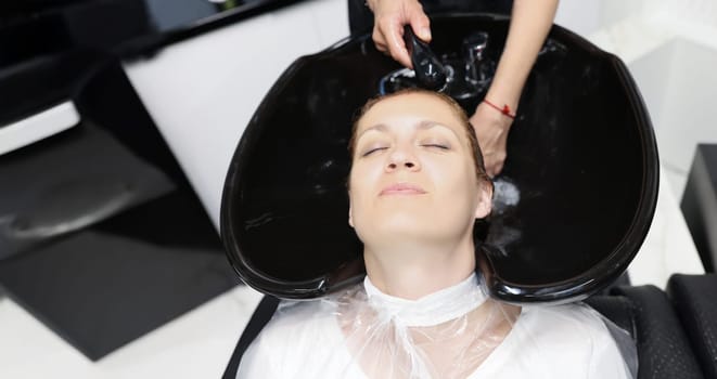 Portrait of woman feel relax and comfortable while getting hair wash with shampoo and massage in beauty salon. Luxury treatment for hair. Wellness concept