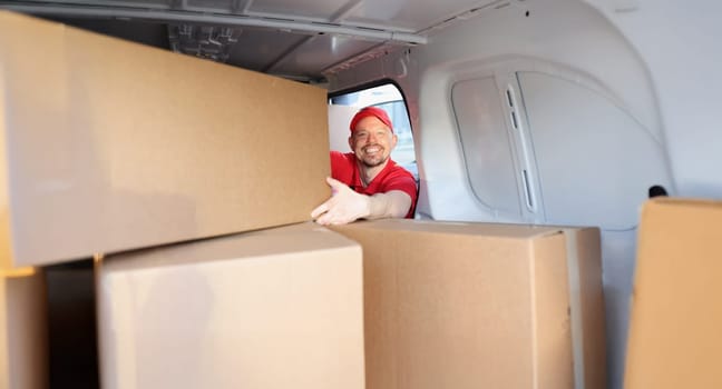Portrait of cheerful man on work put boxes in truck for further delivery on address. Happy man help with relocation and load belongings. Helper concept