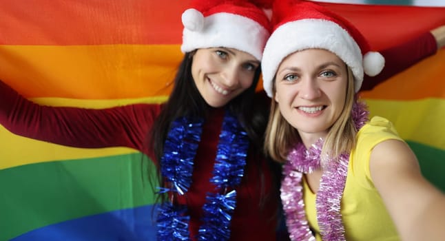 Portrait of female lovers happy about new year celebration hold lgbt flag. Smiling couple posing for picture. New year party, christmas, holiday concept