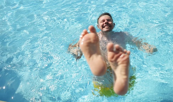 Portrait of man diving into water in swimming pool with feet up. Laughing cheerful middle aged male enjoy summer hot water. Summertime, fun, chill concept