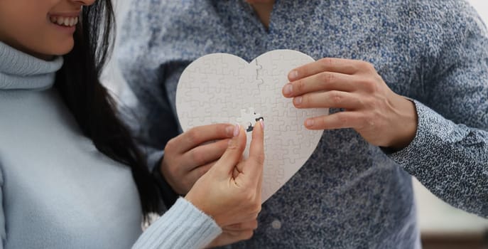 Close-up of woman and man fill empty space with missing piece of white heart puzzle. Find missing detail as symbol for healing broken heart. Love concept