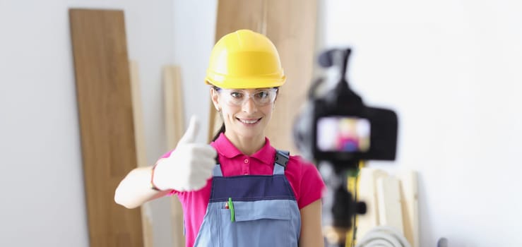 Portrait of happy woman construction site worker show thumbs up on camera. Film process on camera as educational lesson. Renovation, design, tech concept