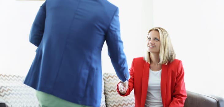 Portrait of attractive young female greeting man with handshake sitting on couch. Business meeting to sign up contract. Deal, agreement, success concept