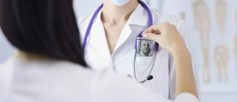 Close-up of woman patient put banknote in doctors pocket on appointment for better service. Pay to get qualified advice. Corruption in medicine concept