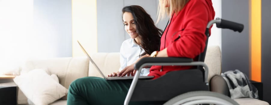 Portrait of best friends spend time together watching movie on laptop, woman in wheelchair hold device on lap. Disabled people, sisterhood, pastime concept