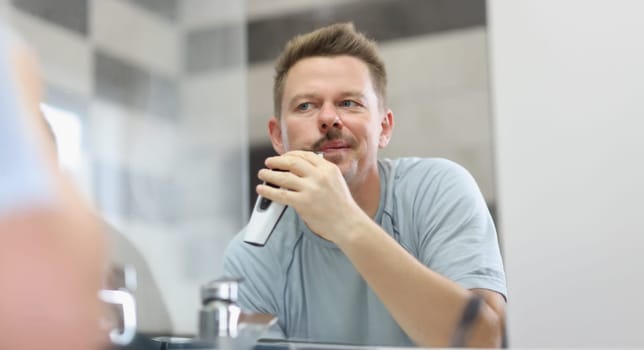 Portrait of middle aged man shaving beard with electronic machine. Device for quick face care, get ready in morning. Good morning, beauty treatment concept