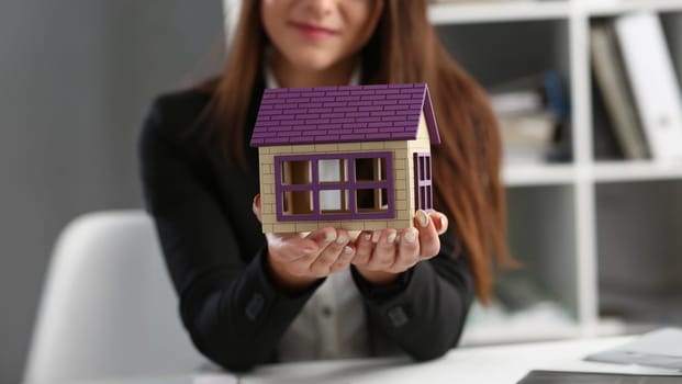 Close-up of woman in office hold miniature toy house in hand symbol of real estate. Sale or rent construction of apartment and housing for families concept