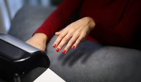 Close-up of woman client putting hand with fresh red nails under lamp to dry it. Spend time on beauty procedure in luxury studio. Beauty, wellness concept