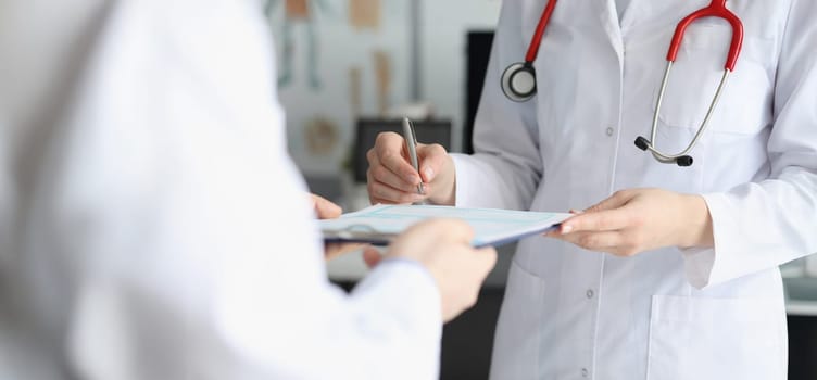 Close-up of doctor in medical gown put sign on clipboard with prescription paper. Qualified worker made prescription for patient. Medicine, clinic concept