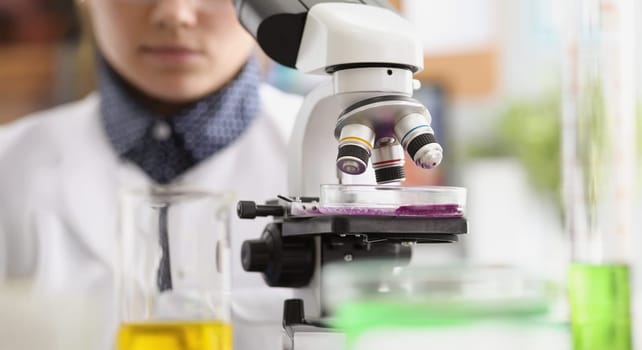 Close-up of woman scientist explore purple sample under microscope in laboratory. Smart chemist or biologist in office. Lab, science, investigation concept