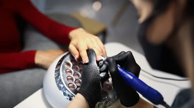 Close-up of nail master use special equipment for working with clients manicure. Professional beauty salon treatment for women. Self care, wellness concept